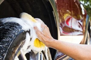 A man washes the tires of his car with a yellow sponge and soap