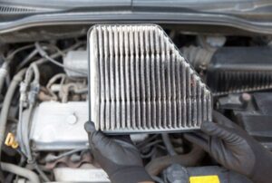 A mechanic holds a dirty, used air filter while spring cleaning a car